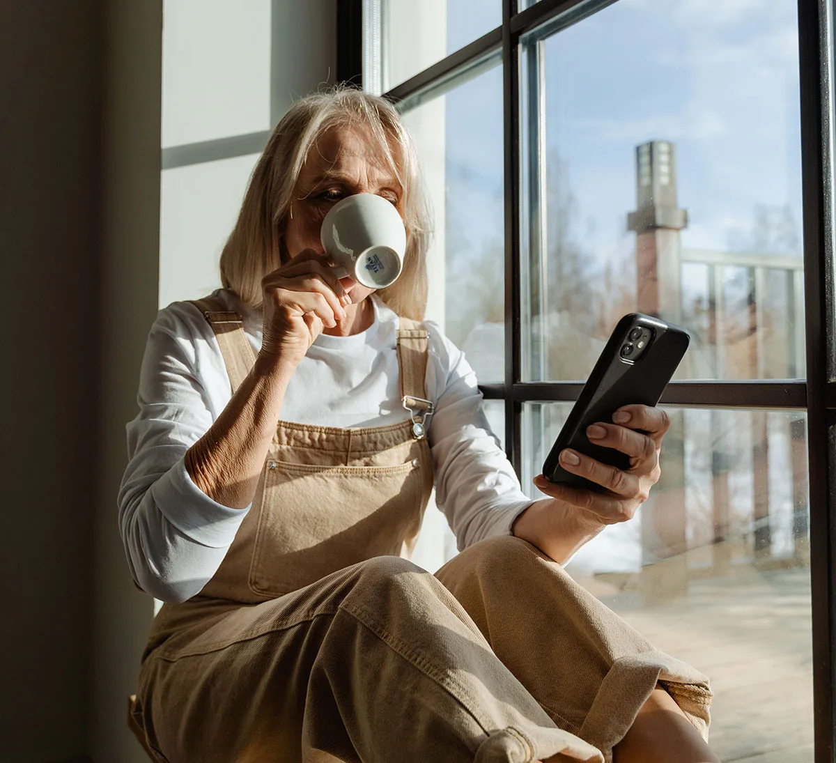 Boende som tittar i mobilen med en kopp kaffe i handen